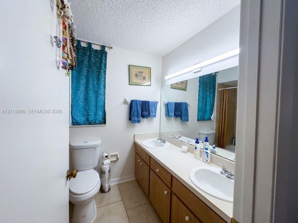 Bathroom featuring a double vanity with integrated oval sinks, solid surface countertop, wood-finish cabinetry, and large wall-mounted mirror with integrated lighting