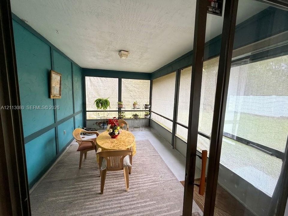 Enclosed sunroom featuring screen-paneled walls, a textured ceiling, dark-tone wall molding, and solid-surface flooring