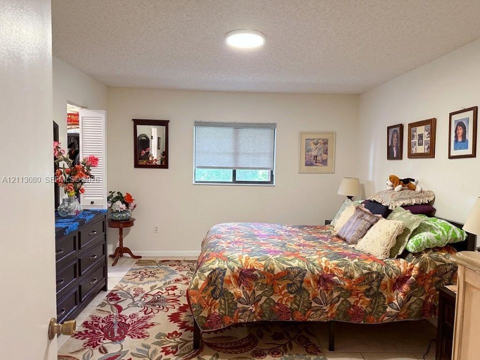 Neutral-toned room featuring a single-hung window with a roller shade, light-colored tile flooring, flush-mount ceiling lighting, and a closet with louvered double doors