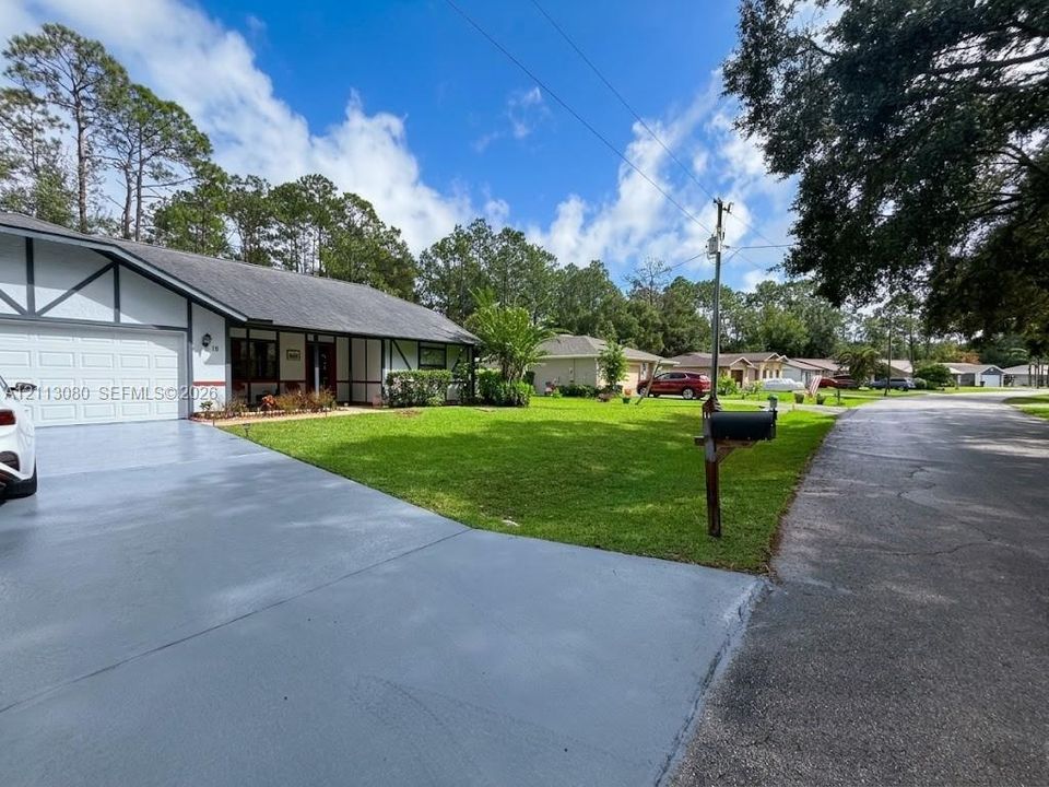 Single-story exterior featuring half-timbered architectural details, a covered front porch, an attached garage, and a expansive front lawn