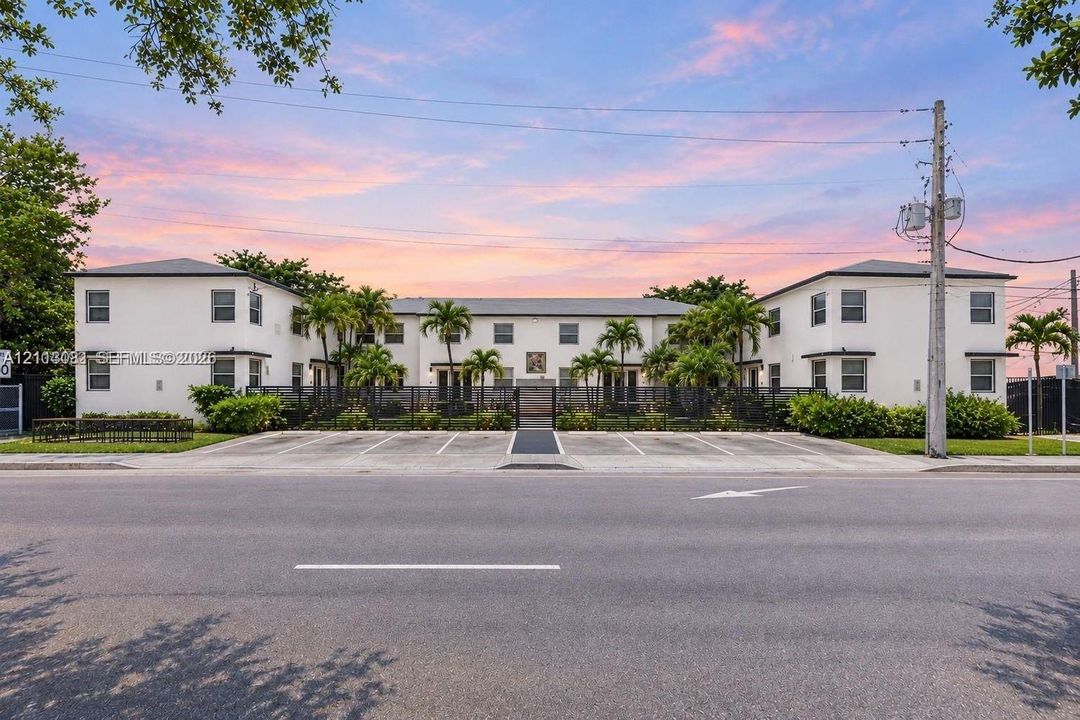 Multi-unit exterior featuring a smooth stucco façade, low-pitched rooflines, integrated surface parking, and manicured palm tree landscaping