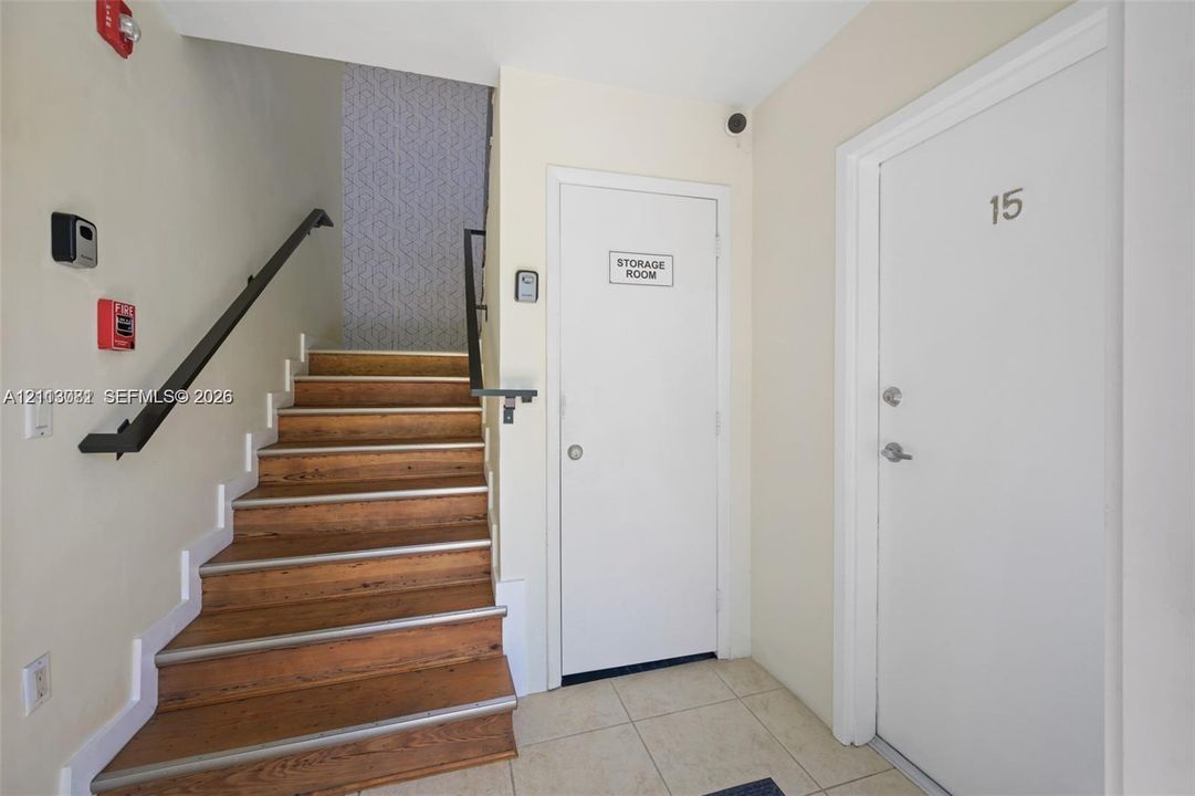 Staircase featuring wood-finish treads and a matte black handrail, accompanied by a dedicated storage room and tile flooring