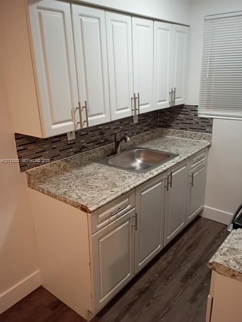 Kitchen featuring white shaker-style cabinetry, stone-finish countertops, stainless steel undermount sink, multi-tonal mosaic tile backsplash, and wood-finish flooring