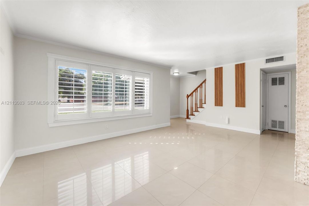 Large-format polished tile flooring, triple-pane plantation shutters, staircase with stained wood handrail, vertical wood-slat wall accents, and textured stone wall finish