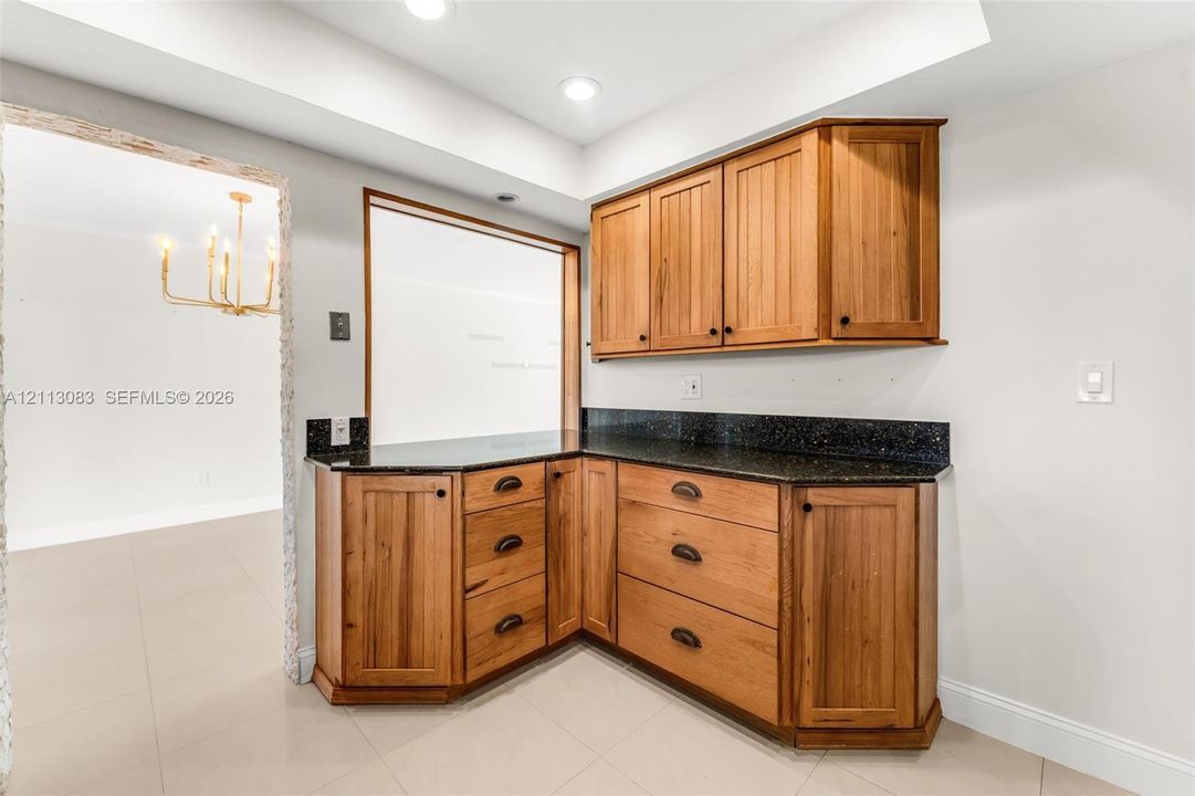 Built-in cabinetry with natural wood finish, dark stone countertops, recessed lighting, and tiled flooring
