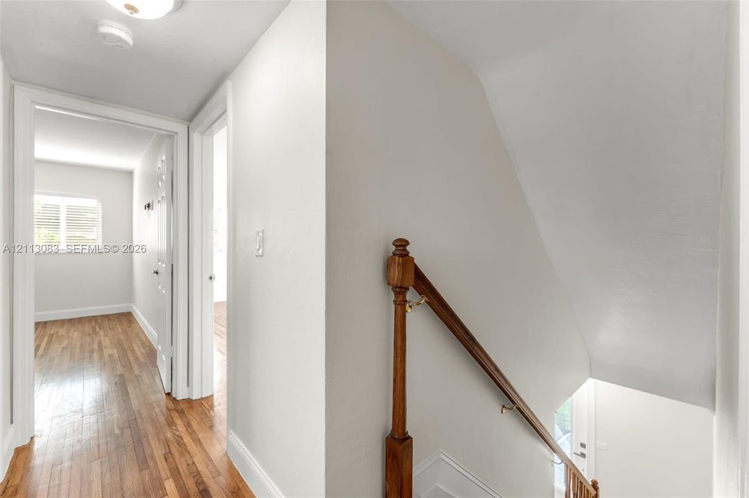 Hallway featuring wood-finish flooring, a wooden staircase railing, and multiple door casings