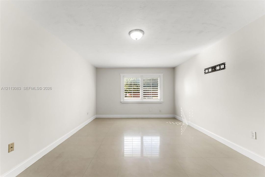 Neutral interior space featuring polished tile flooring, crisp white walls, and a window accented with plantation shutters