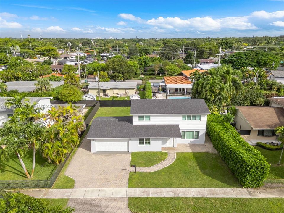 Two-story residence featuring a multi-pitched shingled roof, white exterior siding, paved driveway, paver walkway, and established perimeter landscaping