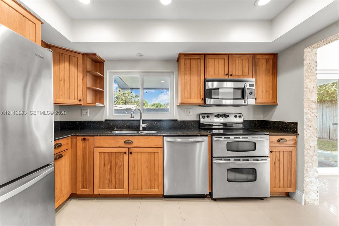 Kitchen featuring wood cabinetry, stone-surface countertops, recessed lighting, and stainless steel appliances including a double-oven range