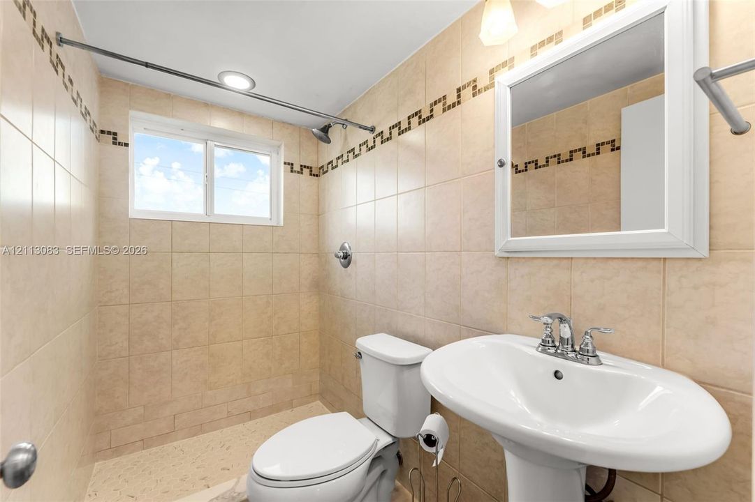 Ceramic wall tiling with mosaic inlay, pedestal sink with chrome faucet, integrated medicine cabinet, and built-in shower fixture