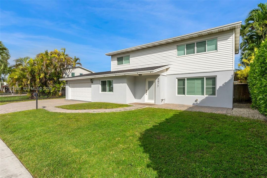 Two-story exterior featuring white horizontal siding, smooth-finish lower facade, attached garage, paver walkway, and impact-resistant windows with shutters
