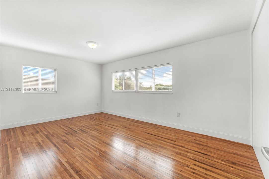 Neutral-toned room featuring wood-finish flooring, white walls, and multiple windows with horizontal blinds