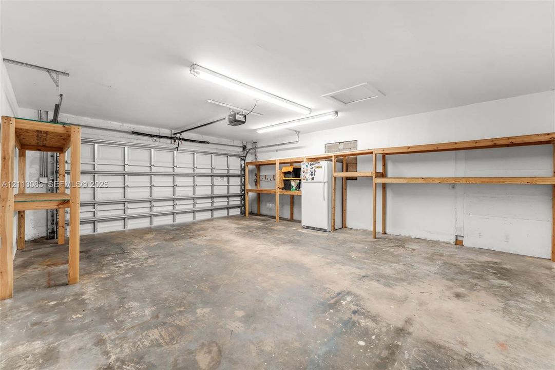 Garage featuring finished concrete flooring, linear fluorescent lighting, and extensive wall-mounted wood shelving