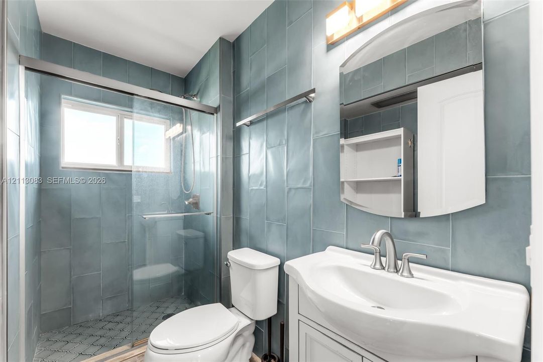 Full-height blue subway tile wall surfacing, walk-in shower with glass enclosure, white vanity cabinet with integrated sink, polished metal faucet fixtures, and wall-mounted vanity mirror
