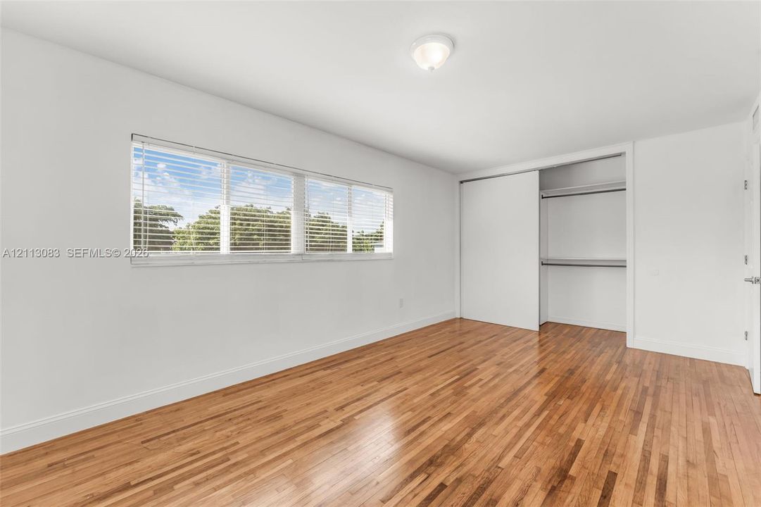 Room featuring wood-finish flooring, a large horizontal window, and a built-in closet with sliding doors