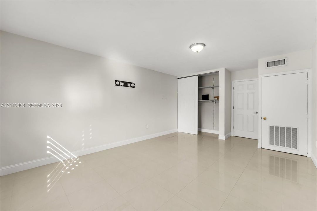 Neutral-toned interior featuring large-format tile flooring, a walk-in closet with built-in shelving, a flush-mount ceiling light, and a six-panel interior door