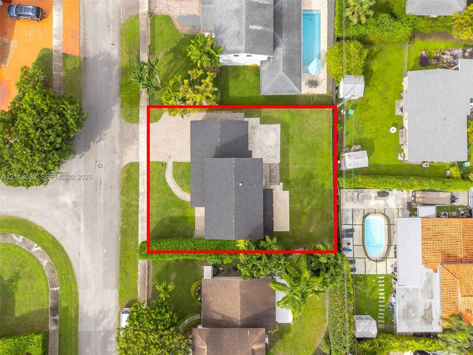 Aerial perspective of the property featuring a paved driveway, a walkway, and a lawn area enclosed by perimeter hedging