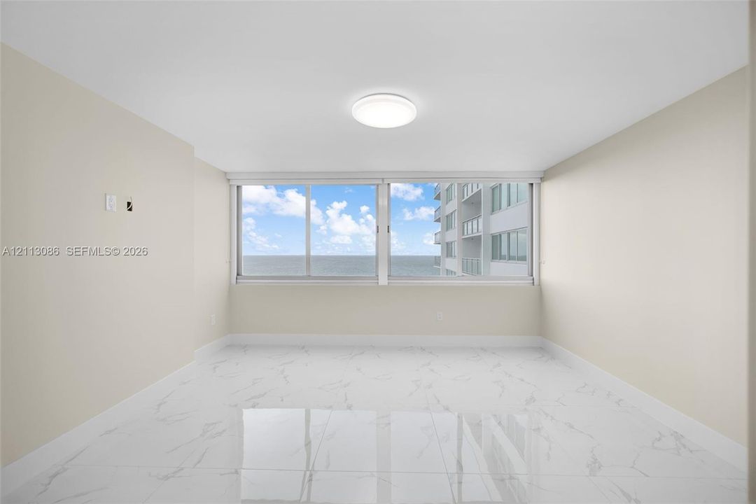 Spacious interior featuring white tile flooring with grey veining, neutral wall tones, large-format sliding windows, and flush-mount ceiling lighting