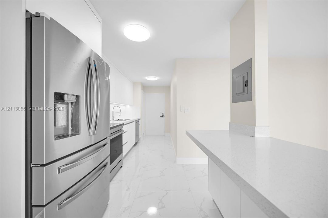 Kitchen featuring stainless steel refrigerator, white cabinetry, solid-surface countertops, and stone-finish tile flooring