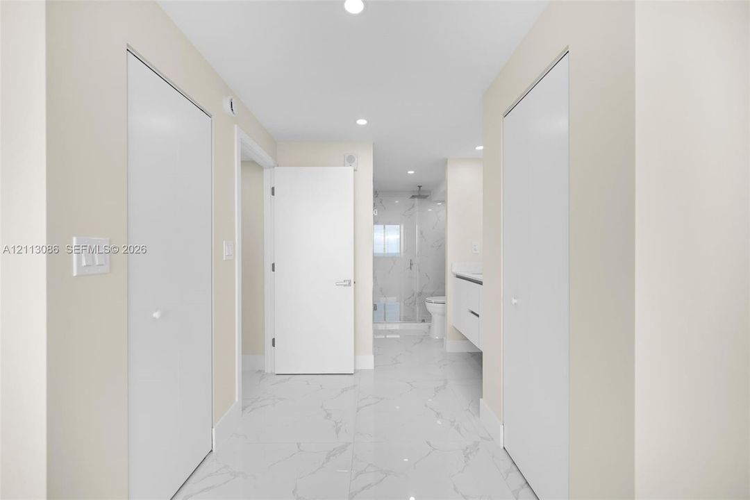 Hallway featuring high-gloss, large-format veined tile flooring, recessed ceiling lighting, dual floor-to-ceiling closets with white doors, and a modern wall-mounted floating vanity