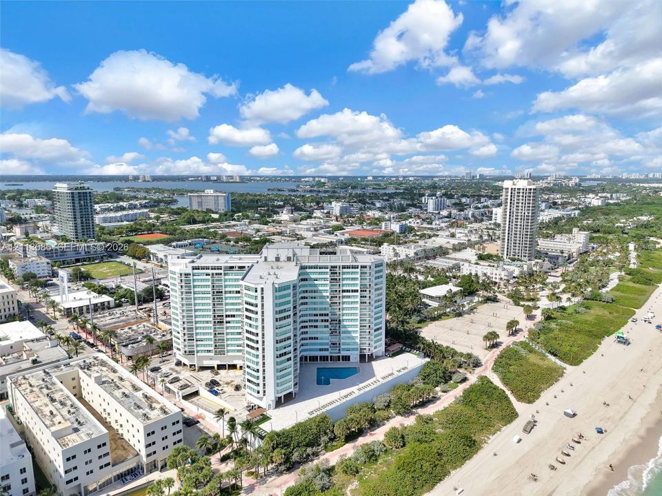 Aerial perspective of a high-rise residential building featuring floor-to-ceiling glass paneling, an outdoor swimming pool, and direct proximity to the coastline