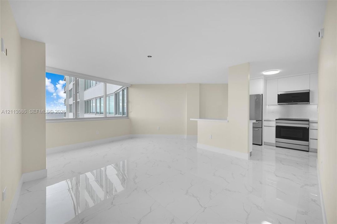 Open-concept living space featuring large-format tile flooring, expansive floor-to-ceiling windows, and a peninsula kitchen with white cabinetry and stainless steel appliances