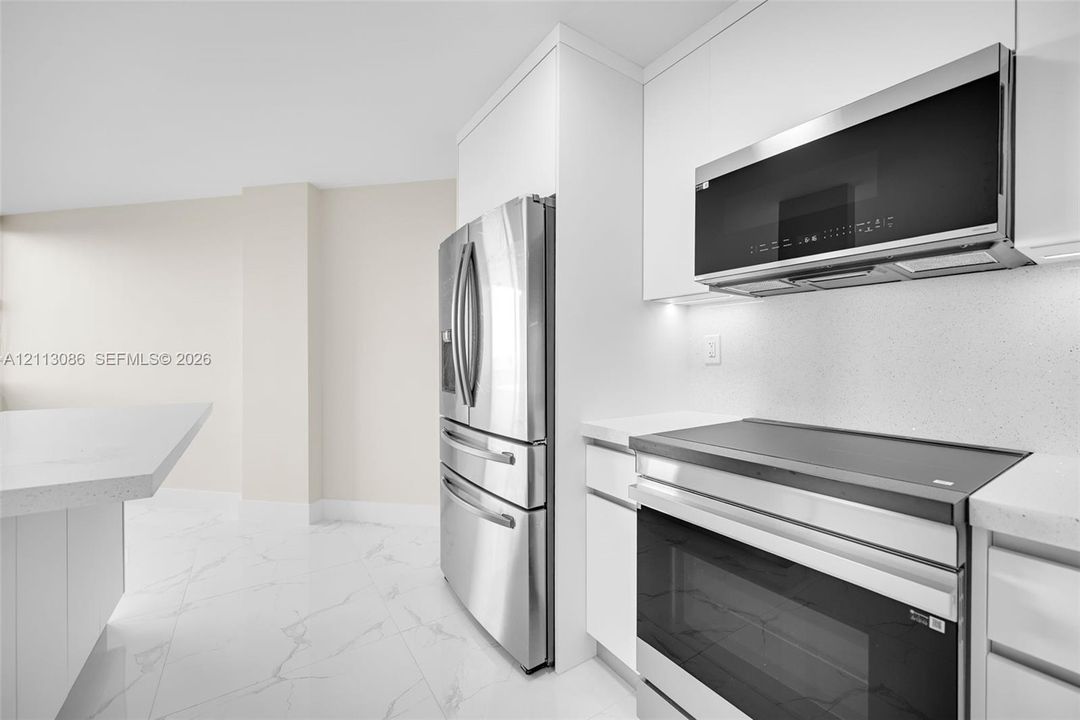Kitchen featuring white flat-panel cabinetry, light-toned stone-surface countertops, stainless steel appliances, and large-format porcelain tile flooring