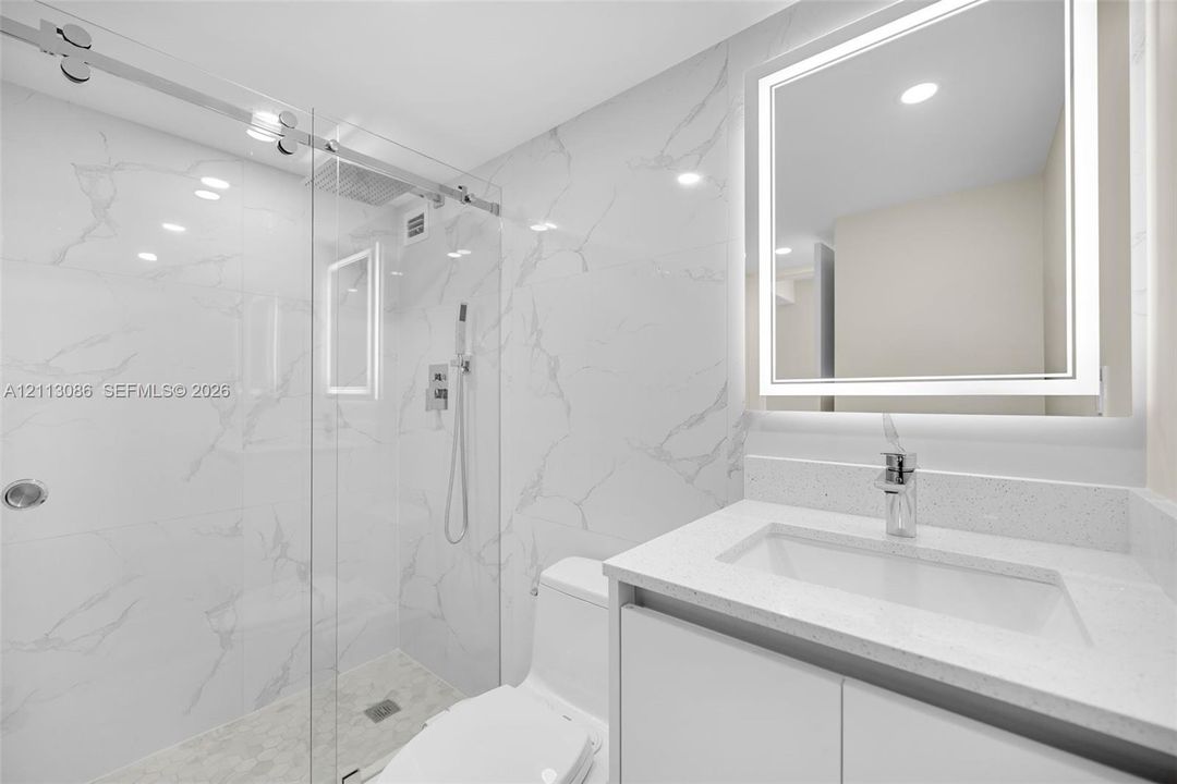 Bathroom featuring a glass-enclosed walk-in shower with stone-finish wall tile, a stone-composite countertop, a vessel-style sink, and a wall-mounted LED mirror