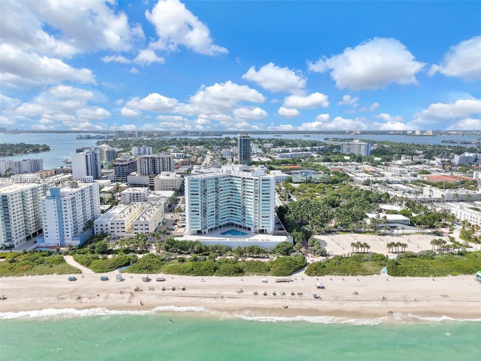 High-rise building featuring a curved architectural design, expansive oceanfront proximity, ground-level outdoor swimming pool, and direct access to sandy beach terrain