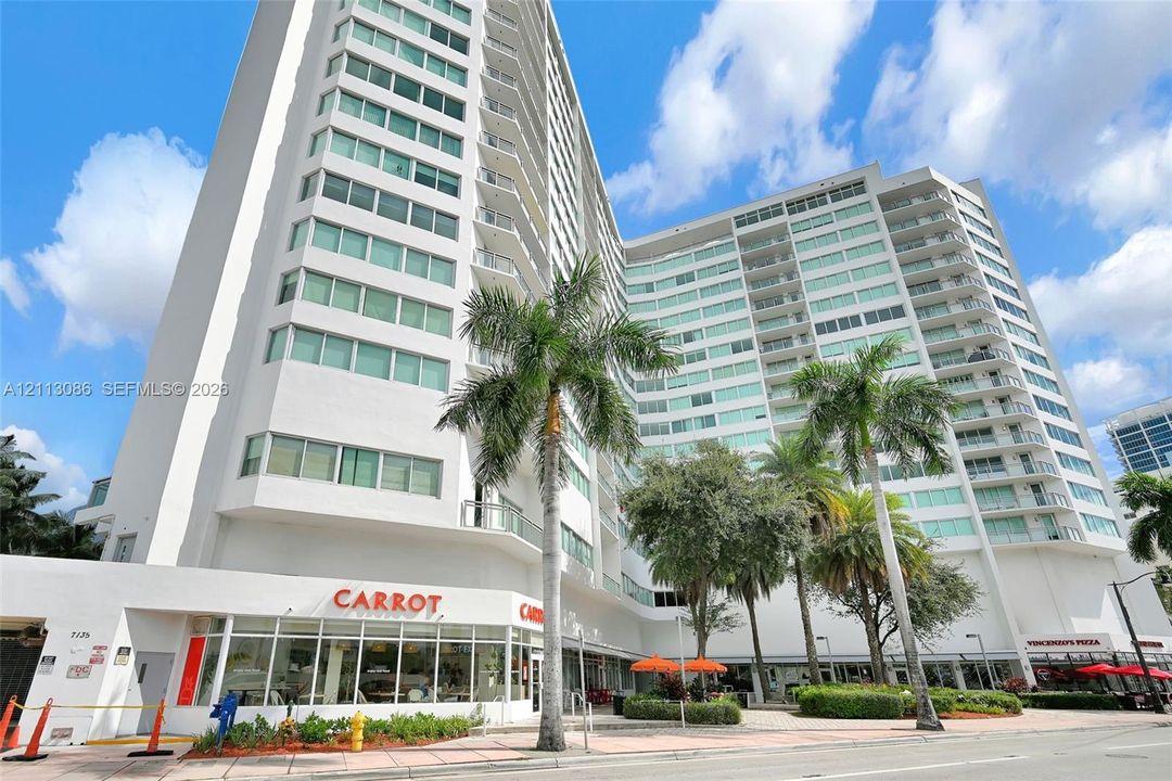 High-rise residential building featuring a white facade, extensive glass window panels, wrap-around private balconies, and ground-level commercial storefronts