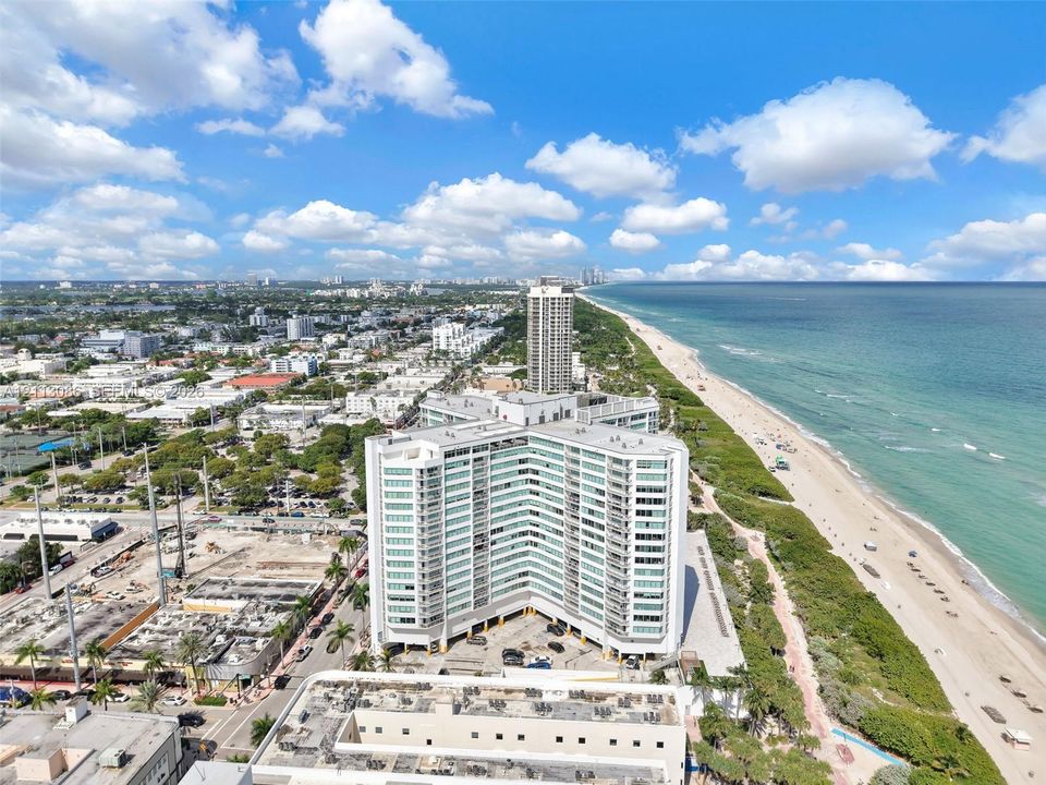 High-rise condominium building featuring a multi-wing architectural design, expansive glass balcony systems, covered ground-level parking, and immediate proximity to the Atlantic coastline