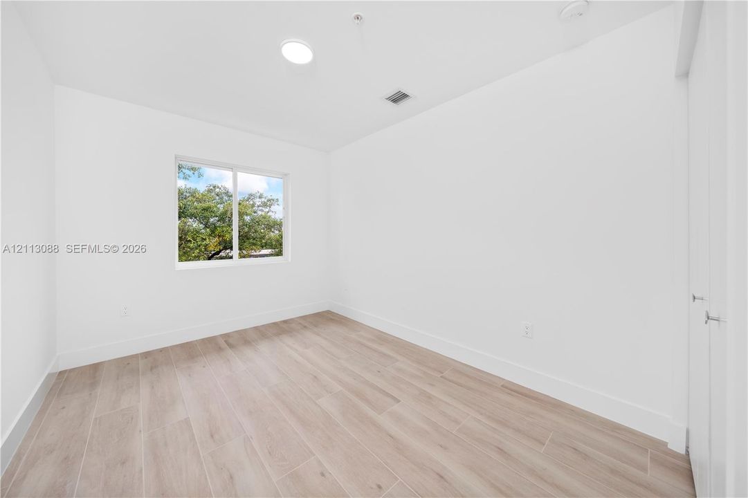 Neutral interior room featuring wood-finish flooring, a flush-mount ceiling light, and a single-pane window with exterior greenery