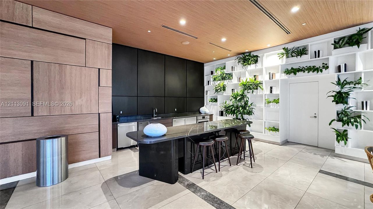 Wood-panel feature wall, matte black cabinetry, stone-surface island, floor-to-ceiling built-in shelving, and large-format tile flooring