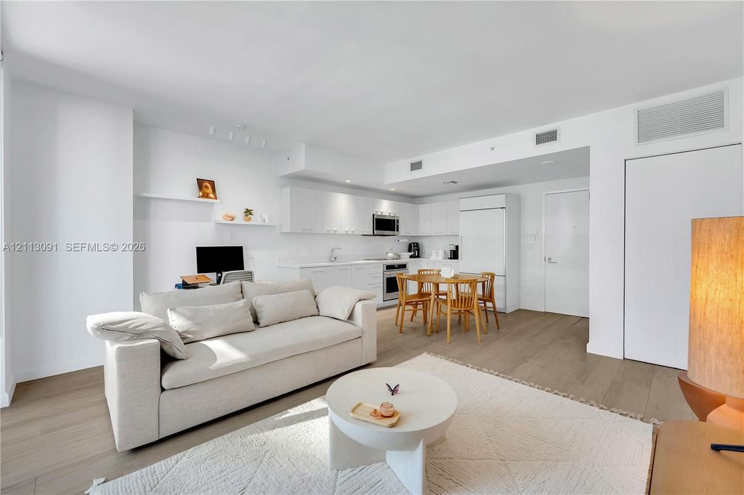 Open-concept kitchen featuring crisp white cabinetry, integrated appliances, built-in shelving, and wood-finish flooring