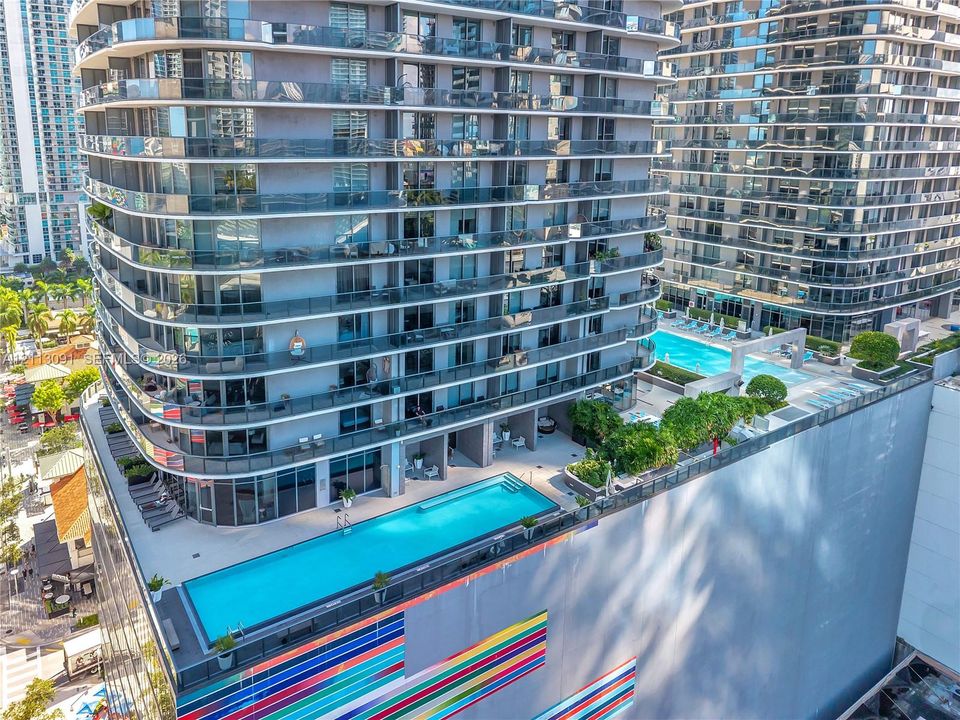 High-rise residential exterior featuring expansive glass-railed balconies and multiple outdoor swimming pools set within landscaped terrace levels