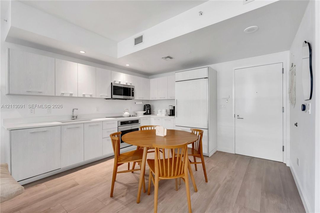 Kitchen featuring flat-panel white cabinetry, solid surface countertops, integrated refrigerator, built-in stainless steel microwave, and wood-finish flooring