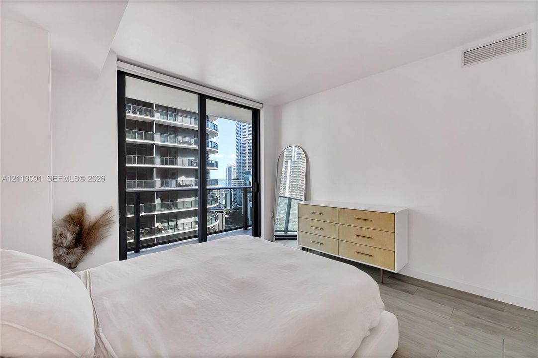 Floor-to-ceiling sliding glass doors, private balcony, wood-finish flooring, and neutral wall tones