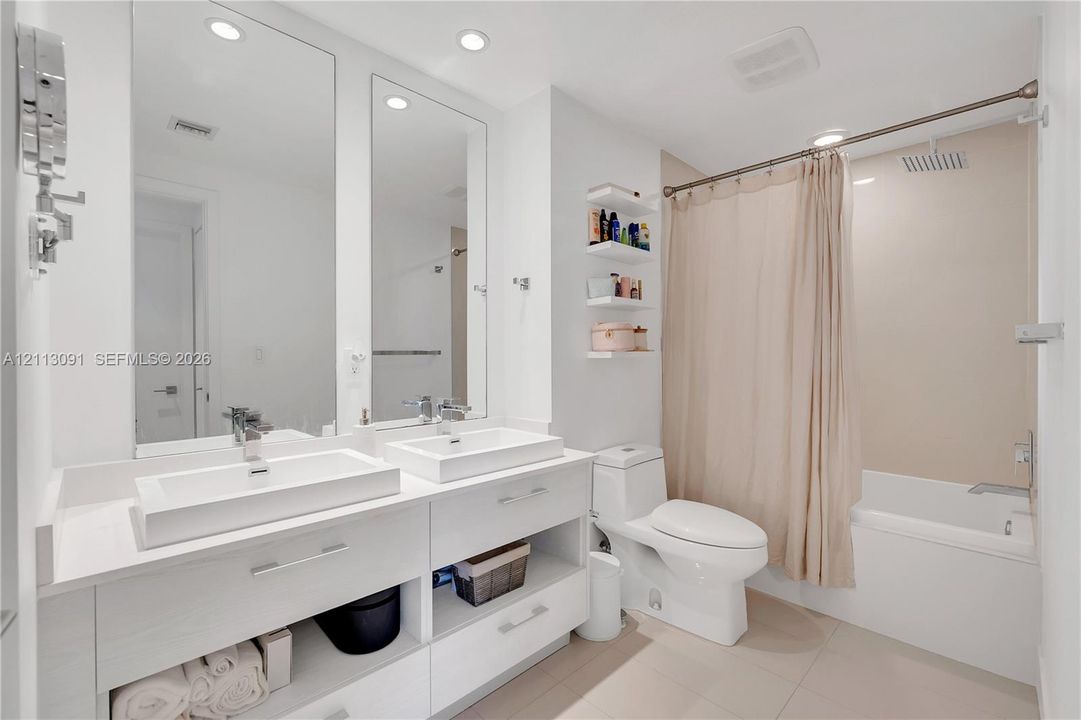 Double vanity featuring rectangular vessel sinks, quartz countertops, integrated under-cabinet shelving, wall-to-wall mirrors, and a tiled shower-tub combination with a rain-style showerhead
