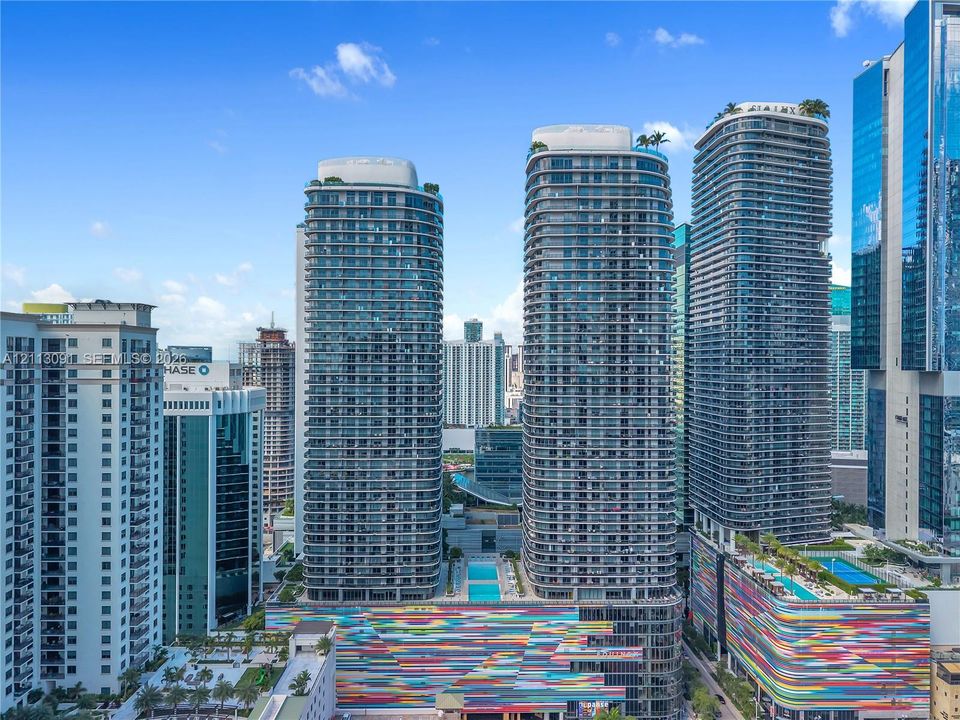 High-rise residential towers featuring glass-paneled balconies, rooftop landscaping, and exterior multi-colored architectural accents, complemented by outdoor swimming pools and terrace areas