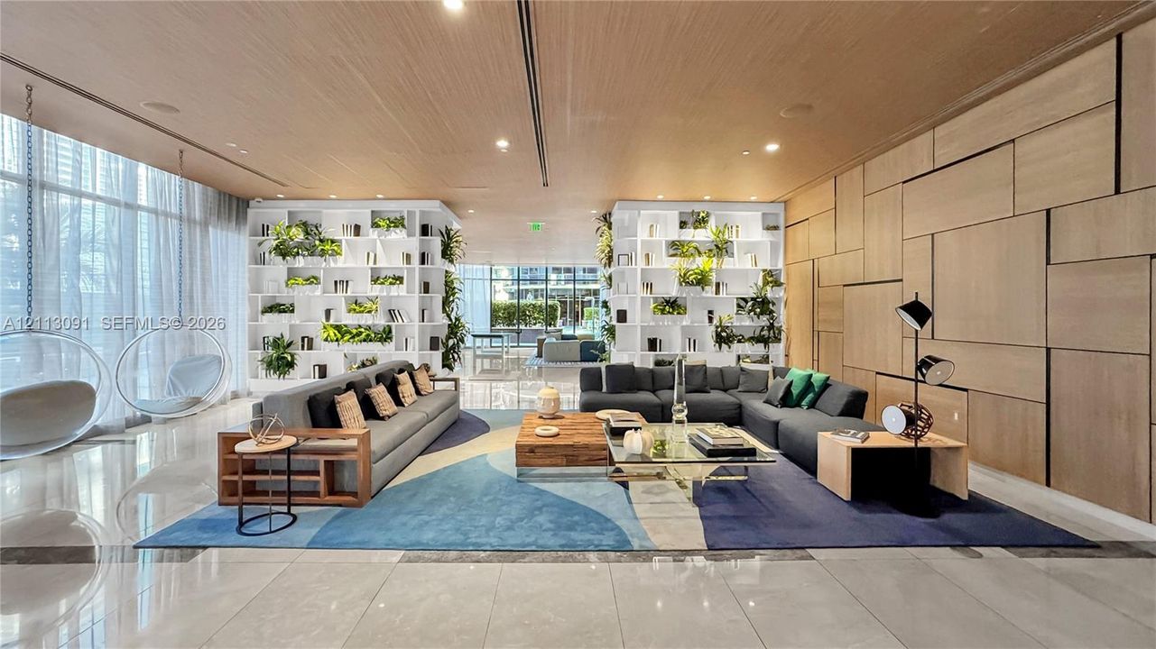 Expansive common area featuring floor-to-ceiling windows, polished stone tile flooring, wood-paneled ceiling, and integrated floor-to-ceiling shelving with built-in planters