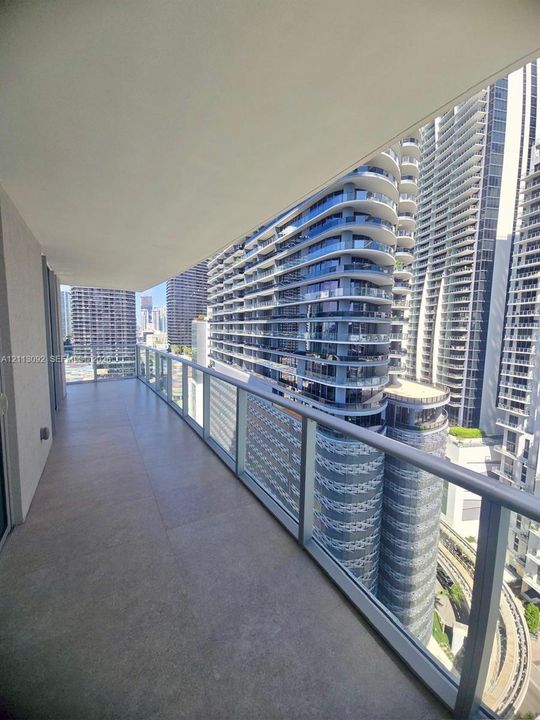 Covered balcony featuring large-format stone-finish flooring and a transparent glass railing with a metal handrail