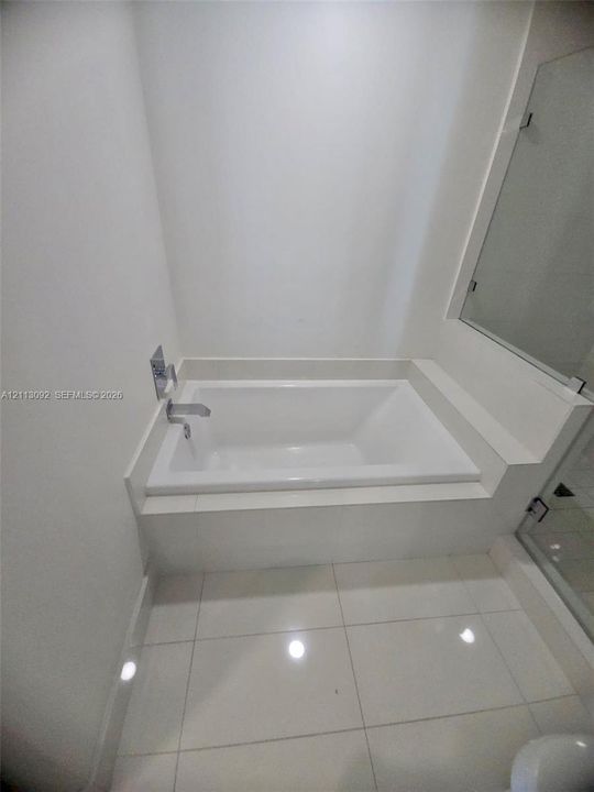 Drop-in soaking tub with a tiled surround, polished chrome wall-mounted faucet, and large-format porcelain tile flooring