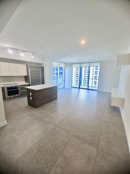 Open-concept interior featuring large-format tile flooring, a kitchen island with a stone-finish countertop, flat-panel cabinetry, built-in stainless steel appliances, and floor-to-ceiling glass paneling