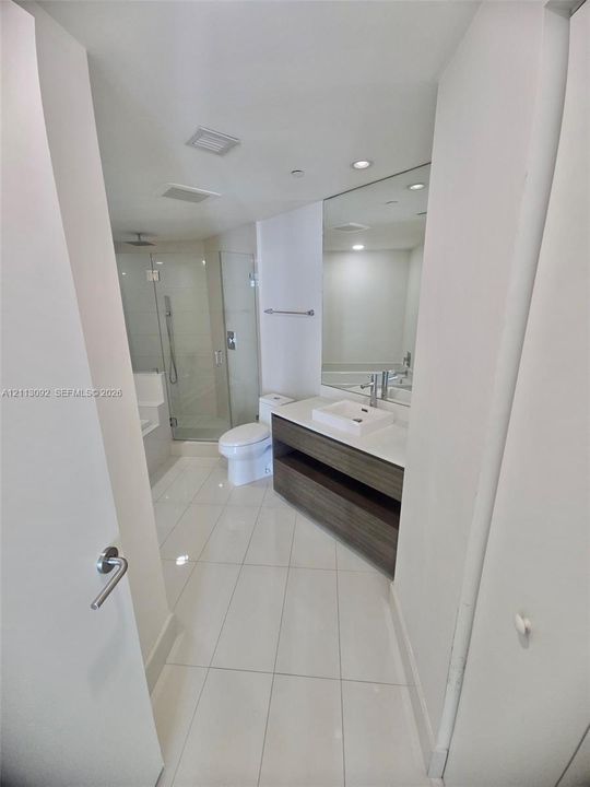 Bathroom featuring a floating vanity with a vessel sink, quartz countertop, glass-enclosed shower, large wall-mounted mirror, and tile flooring