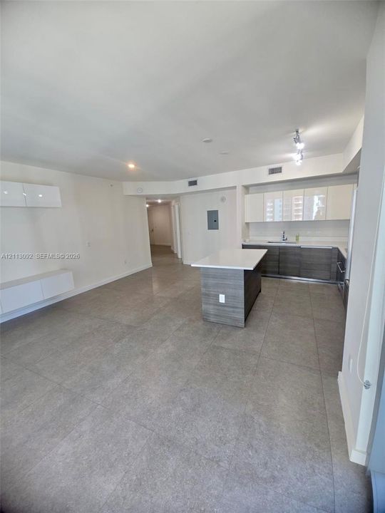 Open-concept kitchen featuring two-tone cabinetry, a central island with a quartz countertop, tile flooring, and integrated wall-mounted storage units