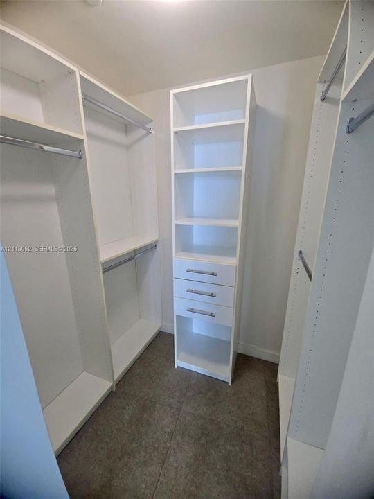 Walk-in closet featuring white built-in shelving, integrated dresser drawers with metallic hardware, and tiered clothing rods
