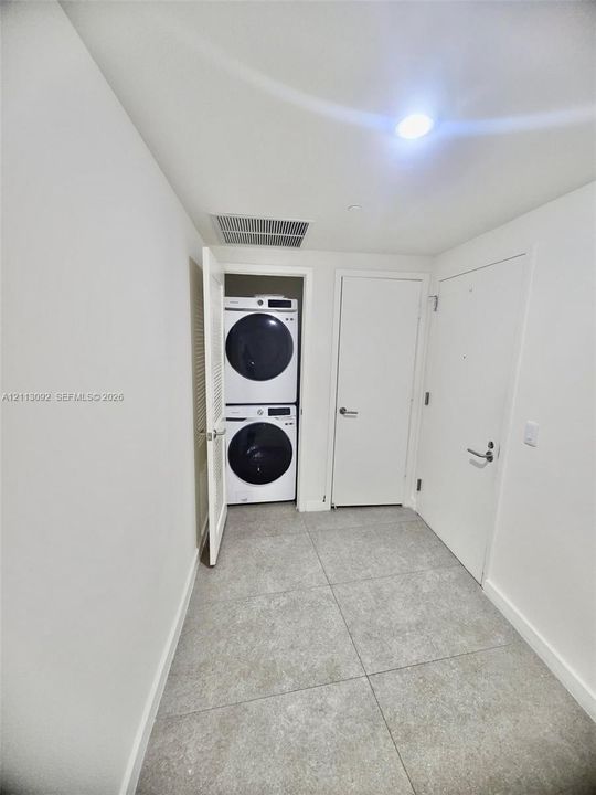 Utility area featuring large-format tile flooring, stackable laundry appliance nook, and solid-core interior doors with satin nickel hardware