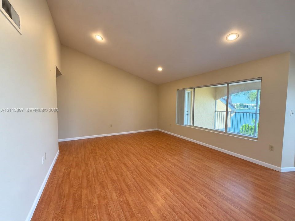 Vaulted ceiling, wood-finish flooring, recessed lighting, and large windows with water exposure