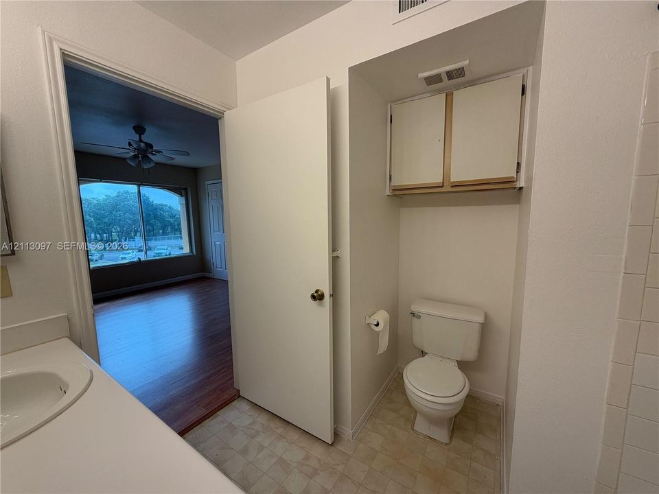 Bathroom featuring a vanity with a white countertop and basin, wall-mounted storage cabinetry, a neutral-toned toilet, and tiled flooring