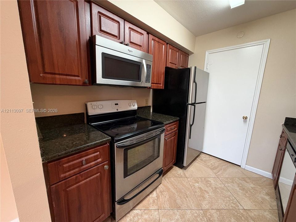 Kitchen featuring wood cabinetry, stone-finish countertops, stainless steel electric range, over-the-range microwave, and tile flooring